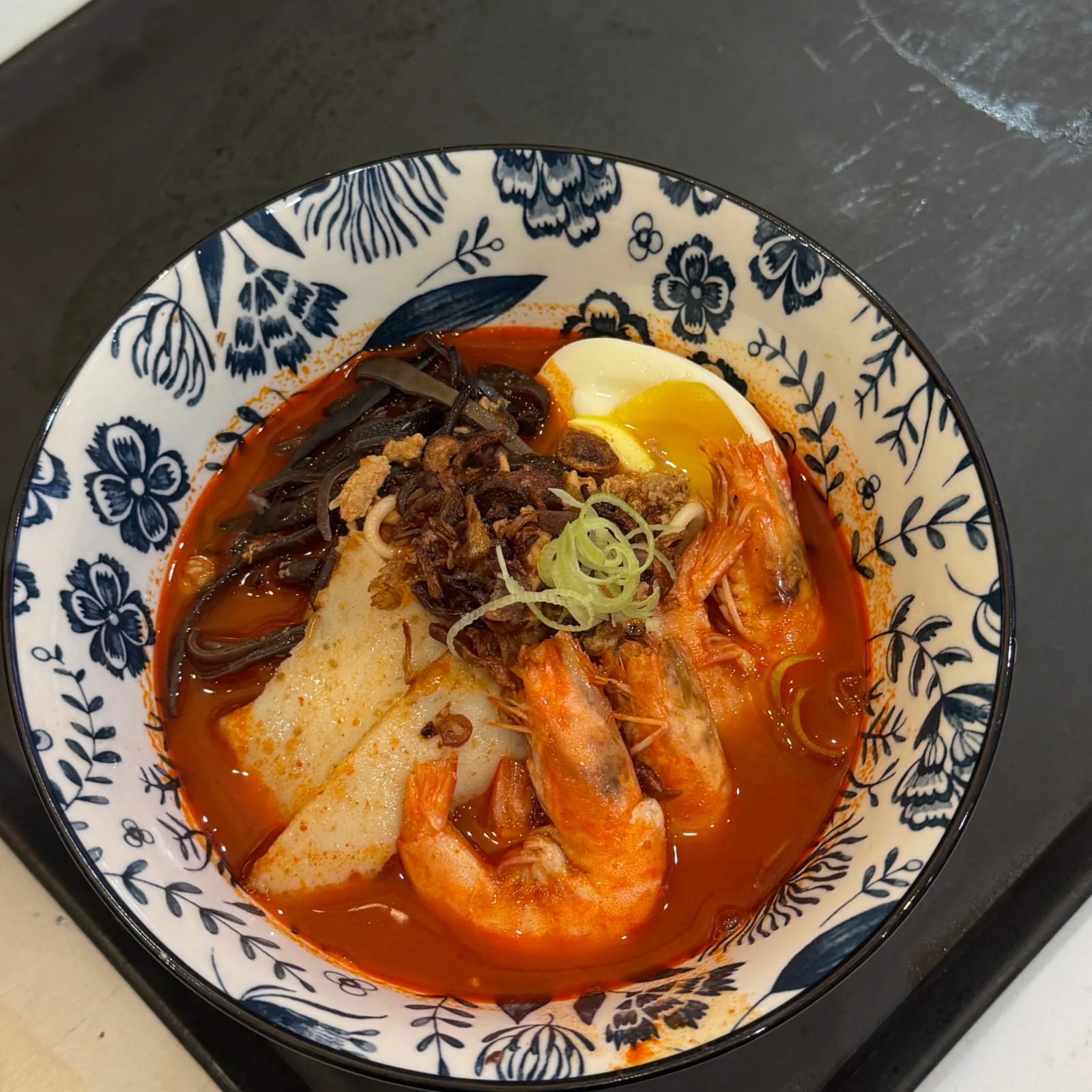 A bowl of spicy prawn ramen with a soft-boiled egg
