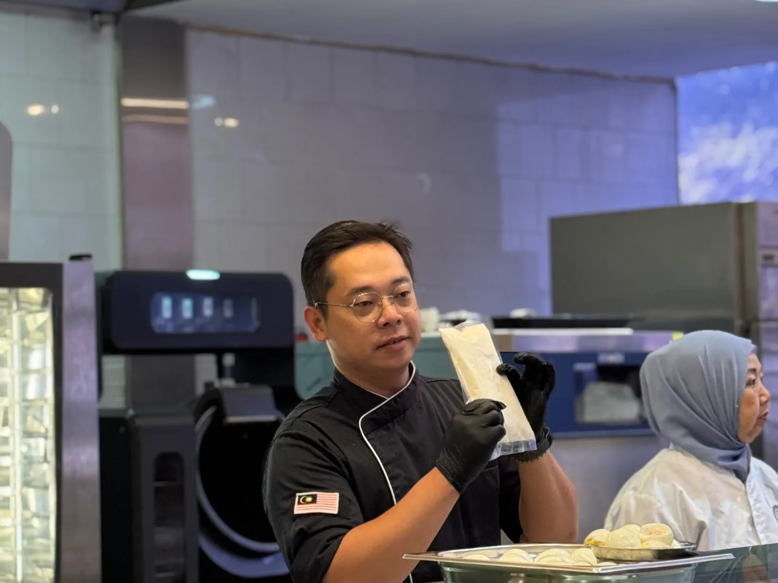 An Ippin chef preparing noodles in the demonstration kitchen, with the Omni Cooking Robot in the background